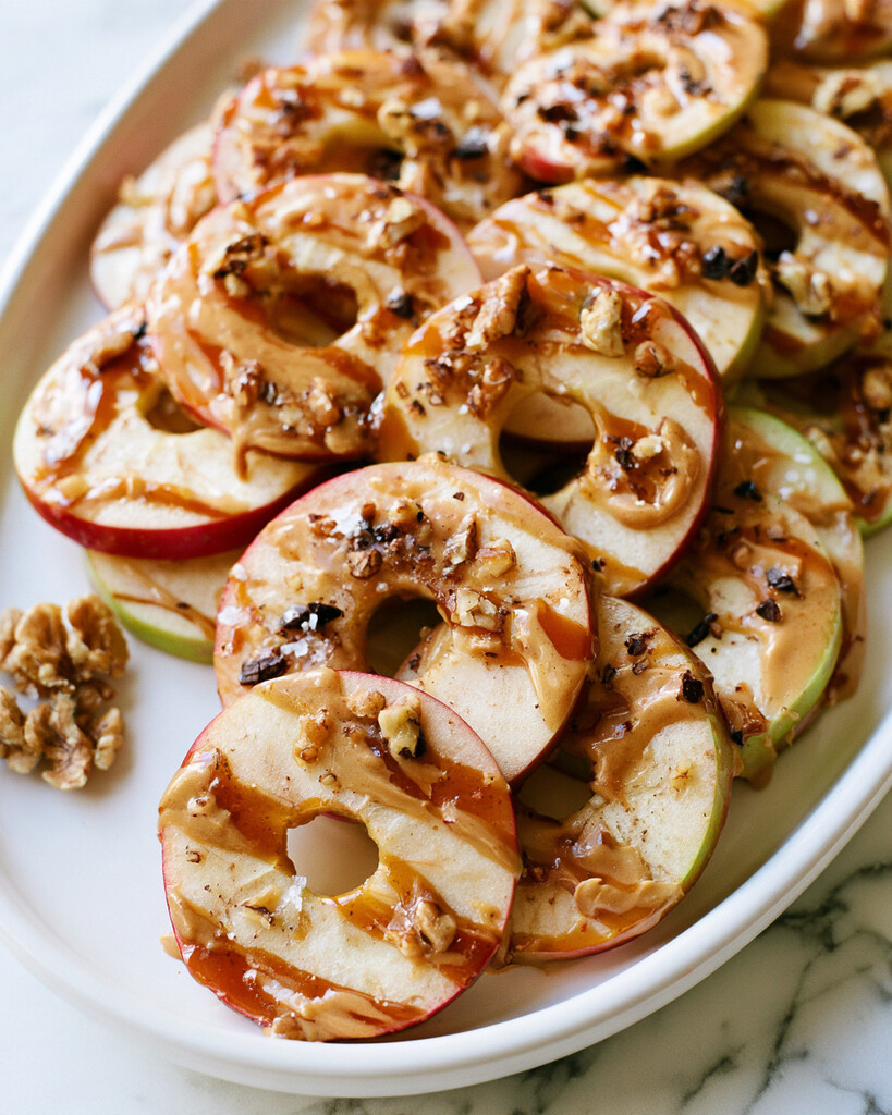 Date caramel apple ring nachos topped with walnuts and chocolate on a white plate