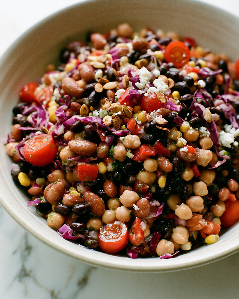 Ceramic bowl filled with cilantro-lime bean salad, loaded with red cabbage, corn, tomatoes, cheese, and pumpkin seeds