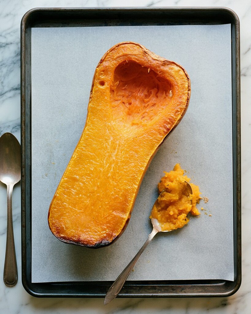 Halved roasted butternut squash on a baking sheet with the center scooped out using a spoon