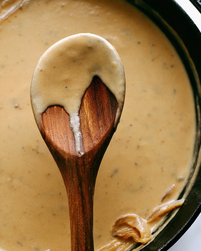 Creamy apple cider sauce coating a wooden spoon in a skillet