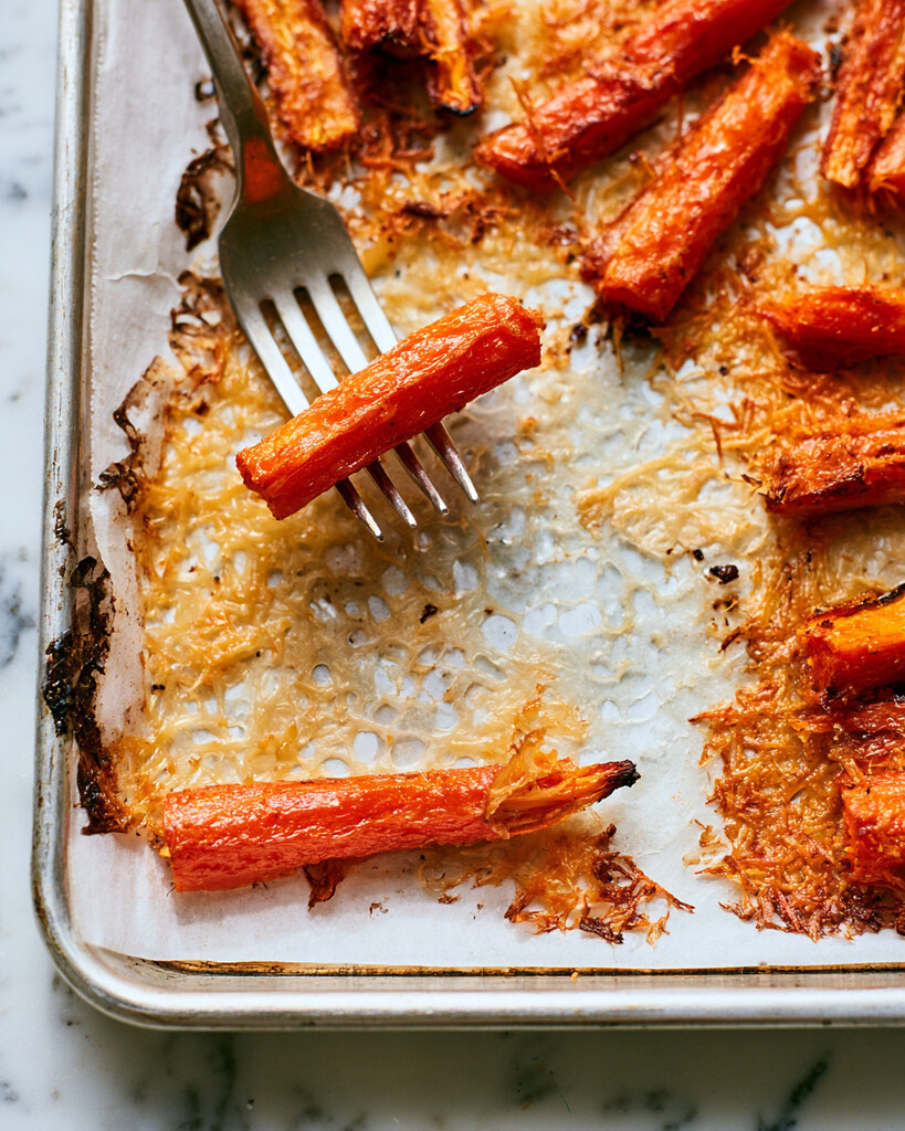 Parmesan-crusted carrots roasting on a parchment-lined baking sheet, developing a golden cheese border