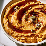 Spreading orange pumpkin hummus into a shallow ceramic bowl with swirling adobo and pumpkin seeds
