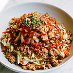 A shallow bowl filled with warm egg roll mixture topped with crispy wontons, green onions, and sriracha