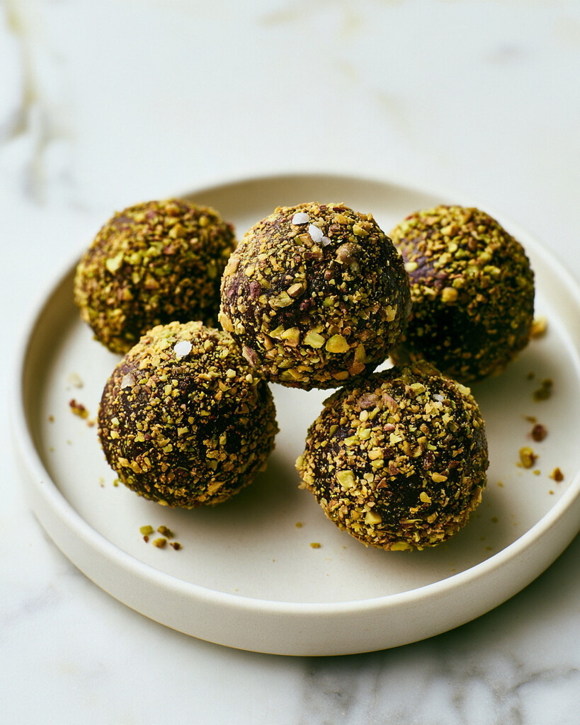 Finished dark chocolate-pistachio energy bites on a ceramic plate, showing their dark crust