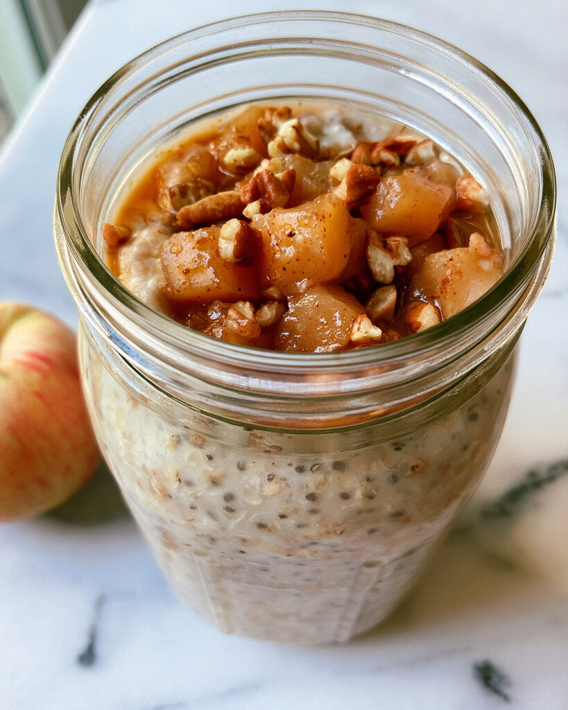 Creamy apple pie overnight oats in a glass jar topped with shiny diced apples and crunchy pecans