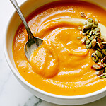 Smooth miso-ginger butternut squash soup inside a white bowl garnished with pumpkin seeds and a cream swirl