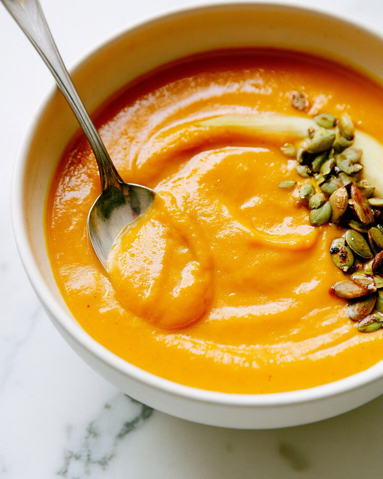 Smooth miso-ginger butternut squash soup inside a white bowl garnished with pumpkin seeds and a cream swirl