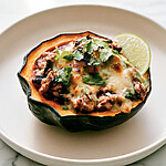 Turkey chili stuffed acorn squash served on a plate with melted cheese and a side of lime