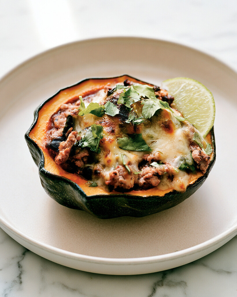 Turkey chili stuffed acorn squash served on a plate with melted cheese and a side of lime