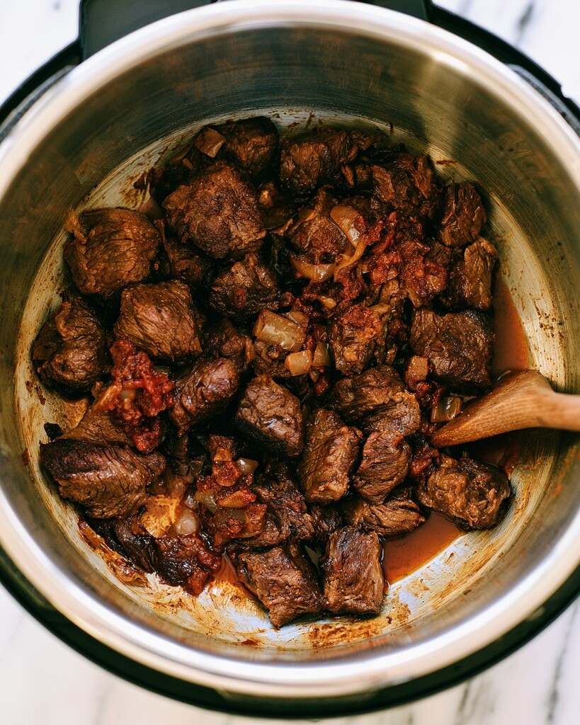 Cubed beef browning with diced onions in the stainless steel insert of a pressure cooker