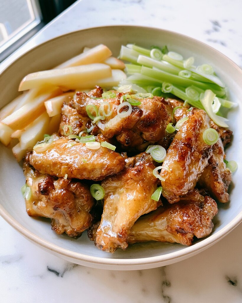 Glossy hot honey and cider-glazed wings plated next to fresh apple, celery, and scallions