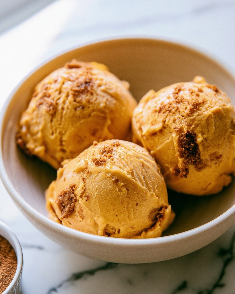 Three tight scoops of pumpkin Biscoff ice cream in a ceramic bowl