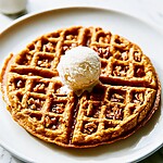 A golden pumpkin oat waffle with crispy edges on a white plate topped with a scoop of ice cream