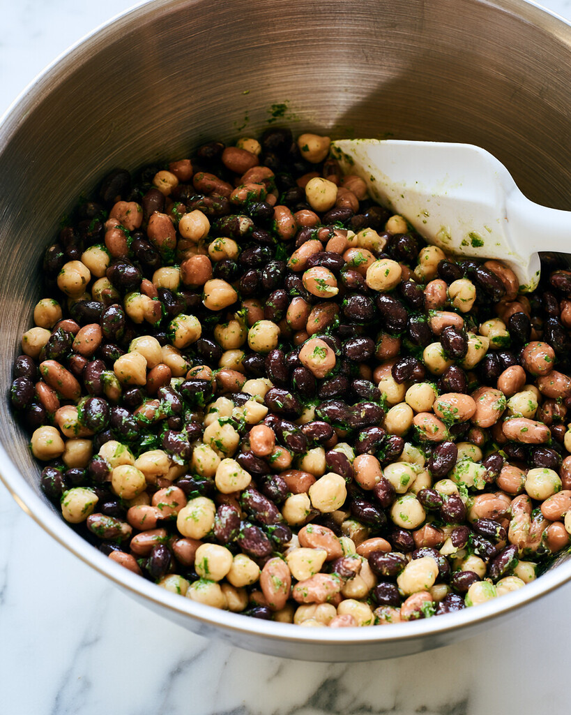 Close-up of black beans, pinto beans, and chickpeas heavily coated in green cilantro-lime dressing