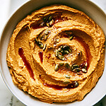 Smooth orange chipotle pumpkin hummus spread in a wide bowl with deep grooves, garnished with an adobo oil swirl and toasted pepitas
