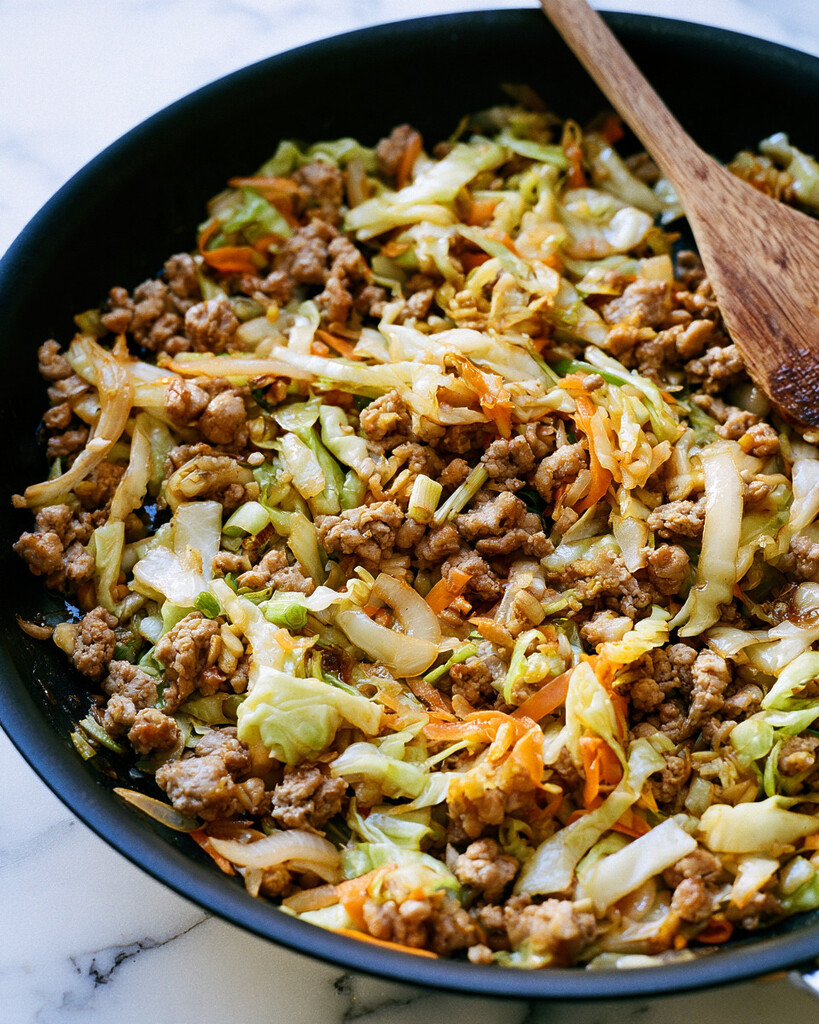 Ground meat crumbles mixing with shredded cabbage and carrots in a dark skillet