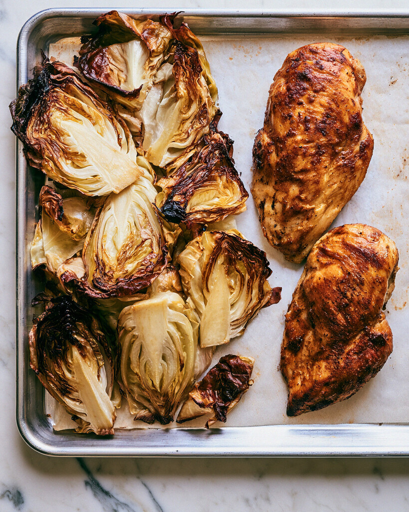 Raw green cabbage and seasoned chicken breasts separated on a foil-lined baking sheet