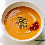 Finished butternut squash soup presented in a white bowl with pepitas and chili oil