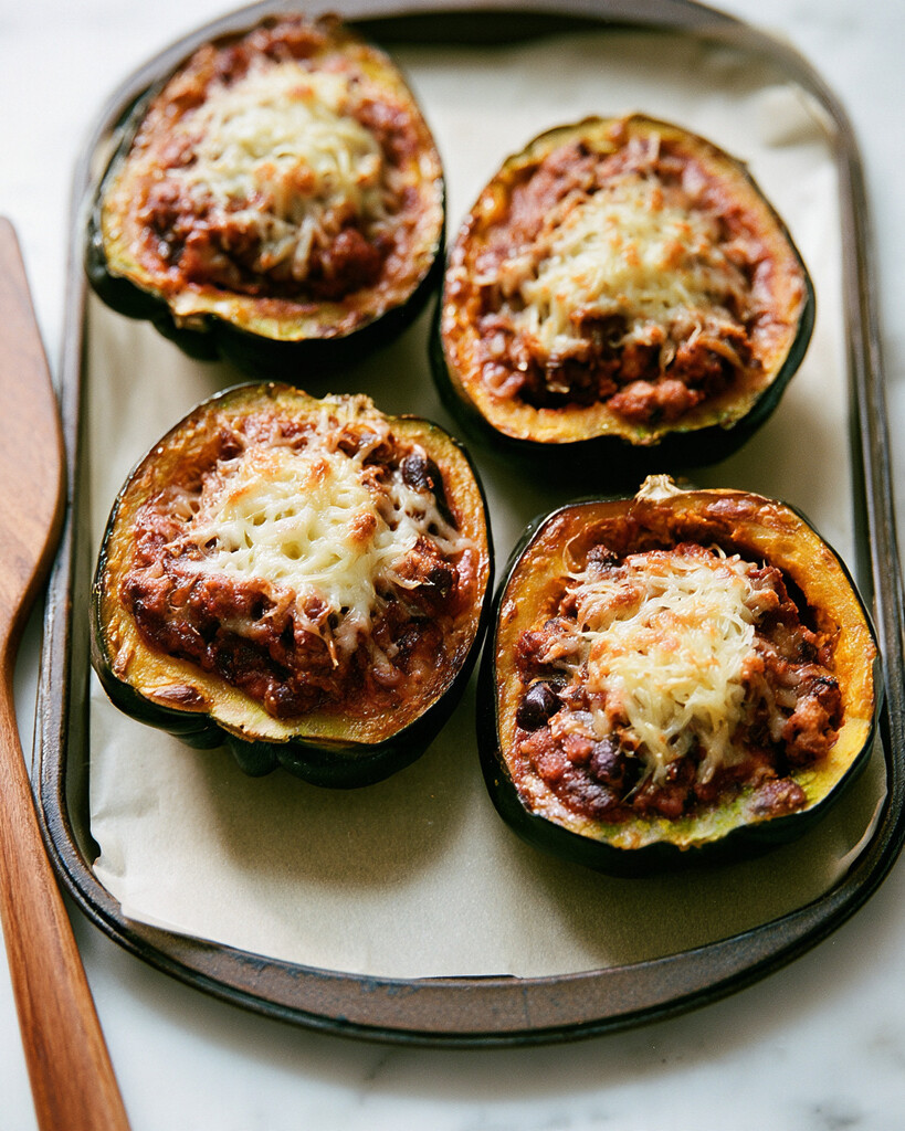 Squash halves filled with turkey chili and topped with melted cheese on a baking sheet