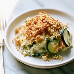 A baked zucchini casserole square on a white plate with a crispy golden stuffing crust and creamy vegetable filling