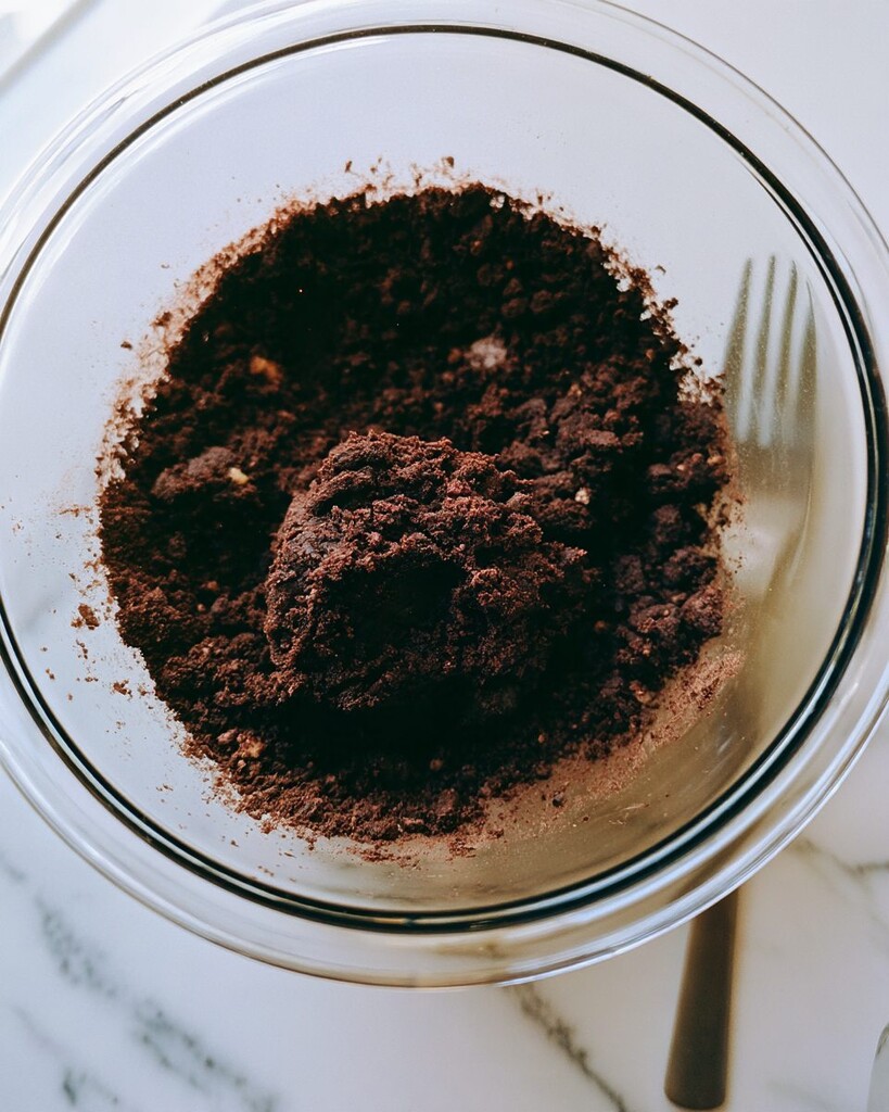Coarse crumbly espresso chocolate pie dough in a glass bowl next to a fork