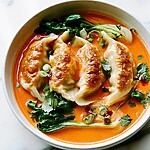 A single serving of baked red curry dumplings with creamy coconut broth and tender greens in a white bowl