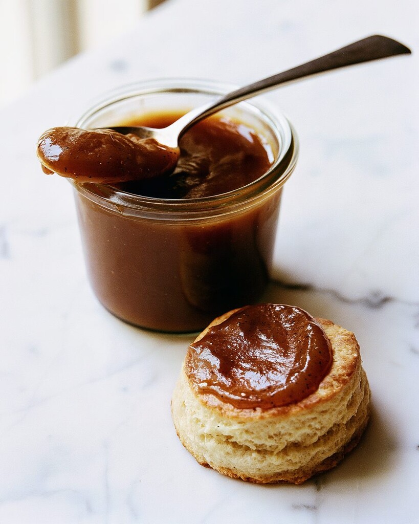 A spoonful of dark apple butter hovering over a glossy biscuit