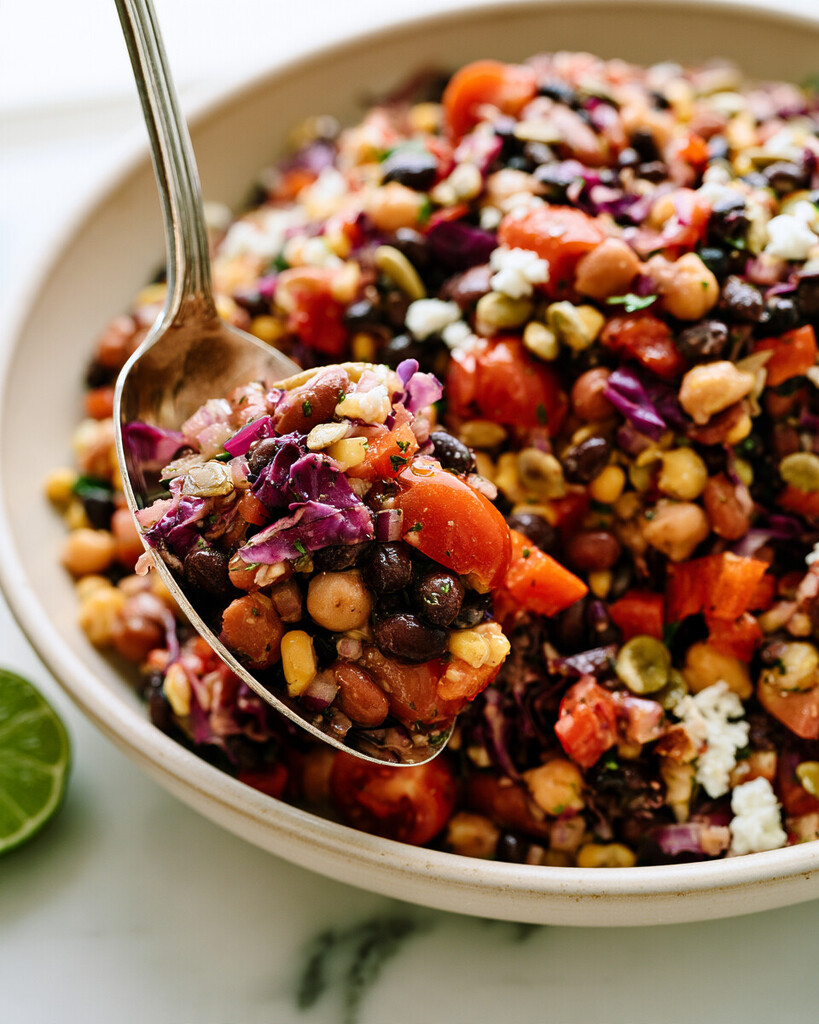 Spoon lifting a cohesive scoop of mixed beans, corn, and chopped vegetables
