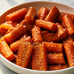 A stack of hot honey Parmesan-crusted carrots in a ceramic dish, showing a reddish-orange color and a lacy, crispy cheese crust
