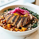 Sliced blackened chicken and pickled onions served over wild rice and kale in a shallow bowl