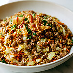 Egg roll in a bowl served in a light ceramic dish with golden cabbage and savory ground meat