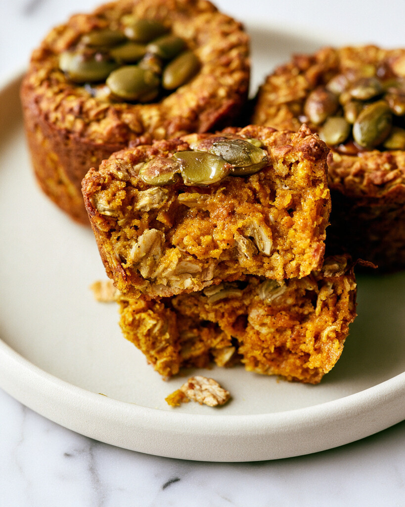 Cut pumpkin baked oatmeal cups on a plate showing a moist orange interior and pumpkin seed topping