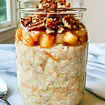 Apple pie overnight oats ready to serve in a glass jar showing layers of oats, fruit, and pecans