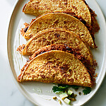 Golden crispy baked pumpkin and black bean tacos on a white plate with diced avocado and fresh cilantro