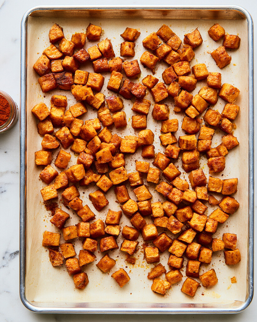 Cubed sweet potatoes coated in spices spread across a parchment-lined baking sheet