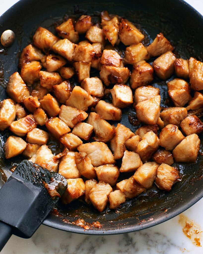 Diced mango chicken browning in a black skillet with a spatula