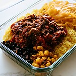 Shredded salsa-braised beef over yellow rice with black beans, corn, and cheddar in a glass container