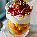 Spiced pear yogurt parfait in a clear glass garnished with red pomegranate seeds and candied nuts