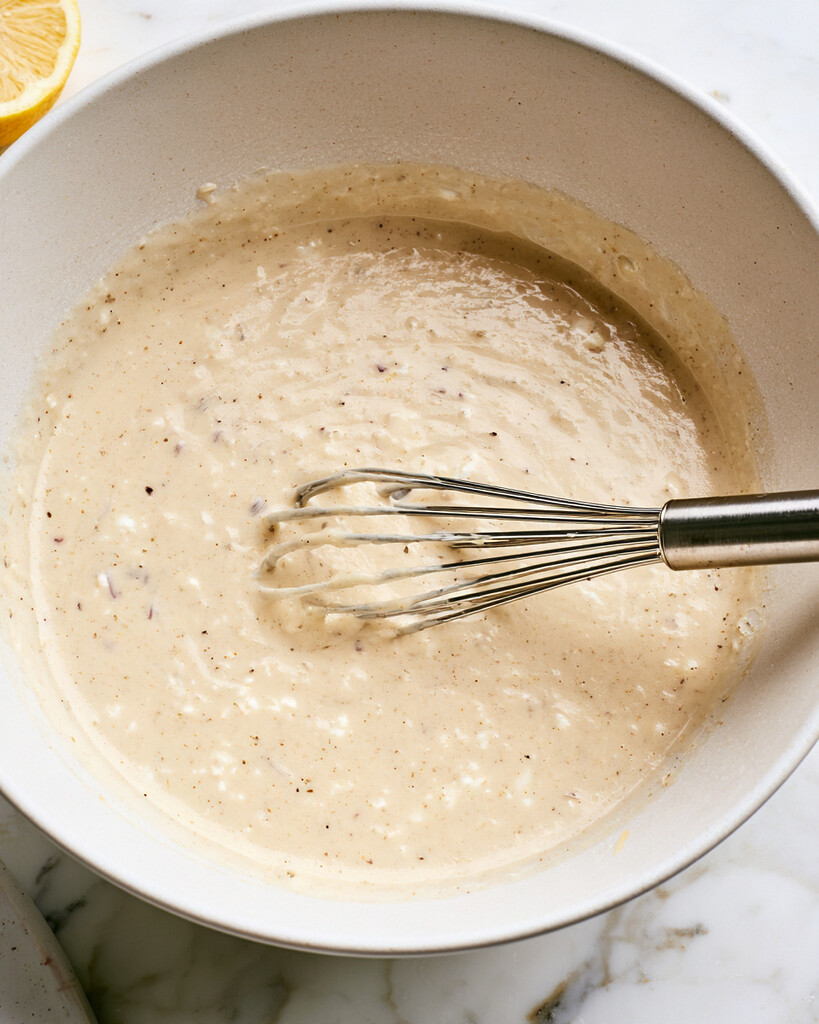 A creamy feta and hot honey dressing whisked in a light bowl with visible black pepper flecks