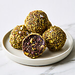 Stacked dark chocolate-pistachio energy bites on a plate with one broken open showing chocolate chips and chia seeds