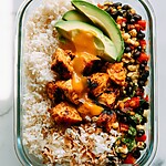 Caramelized mango chicken in a glass container with coconut rice, black bean salsa, avocado, and toasted coconut