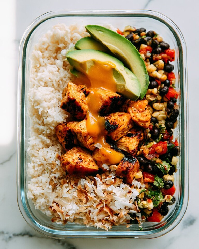 Caramelized mango chicken in a glass container with coconut rice, black bean salsa, avocado, and toasted coconut