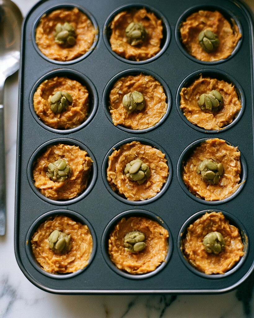 Unbaked pumpkin oatmeal batter portioned into a muffin tin with pumpkin seeds clustered in the center of each
