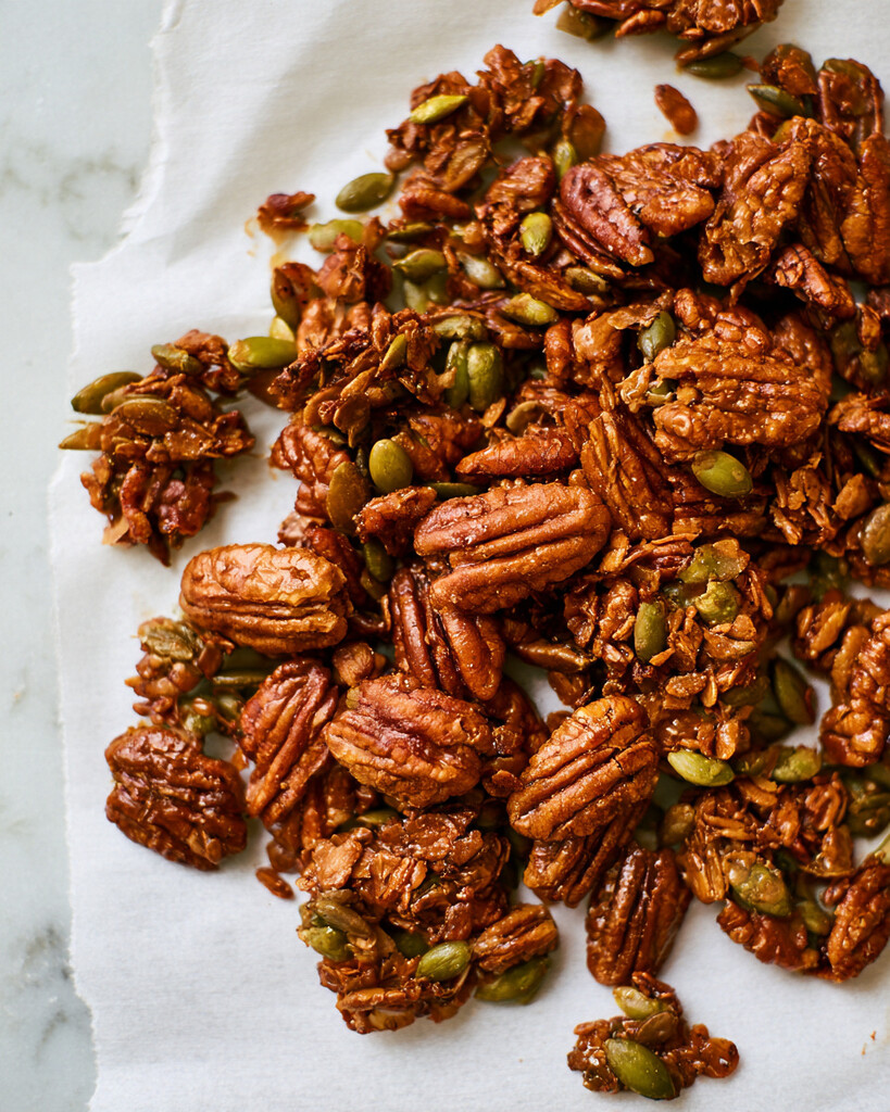 Maple glazed pecans and pumpkin seeds spread out to cool on parchment paper