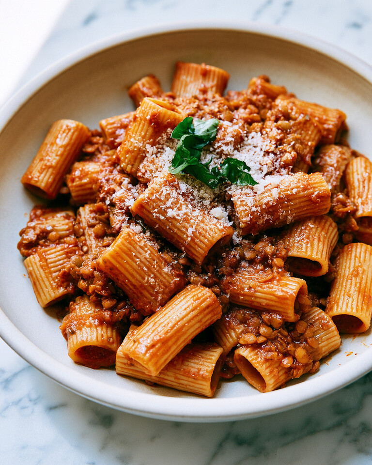 Ceramic plate of balsamic-butter lentil bolognese tossed with rigatoni and topped with grated Parmesan and torn basil