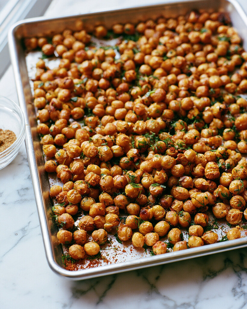 Roasted chickpeas coated in red spices and green herbs on a metal baking sheet