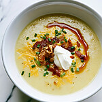 Garlic-butter loaded baked potato soup in a white bowl with cheddar, bacon, sour cream, chives, and a butter swirl
