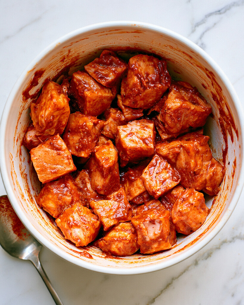 Cubed salmon coated in a thick red blackened spice paste inside a white mixing bowl