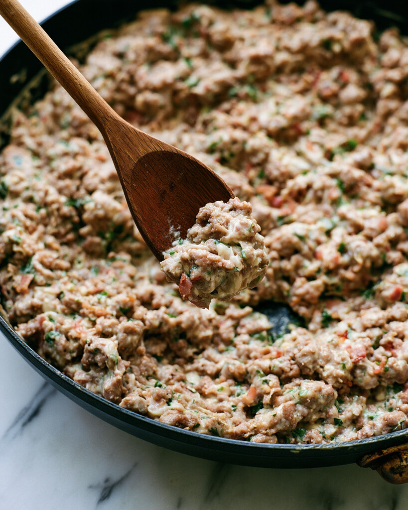 Creamy sausage and bacon filling mixed in a black skillet with a wooden spoon