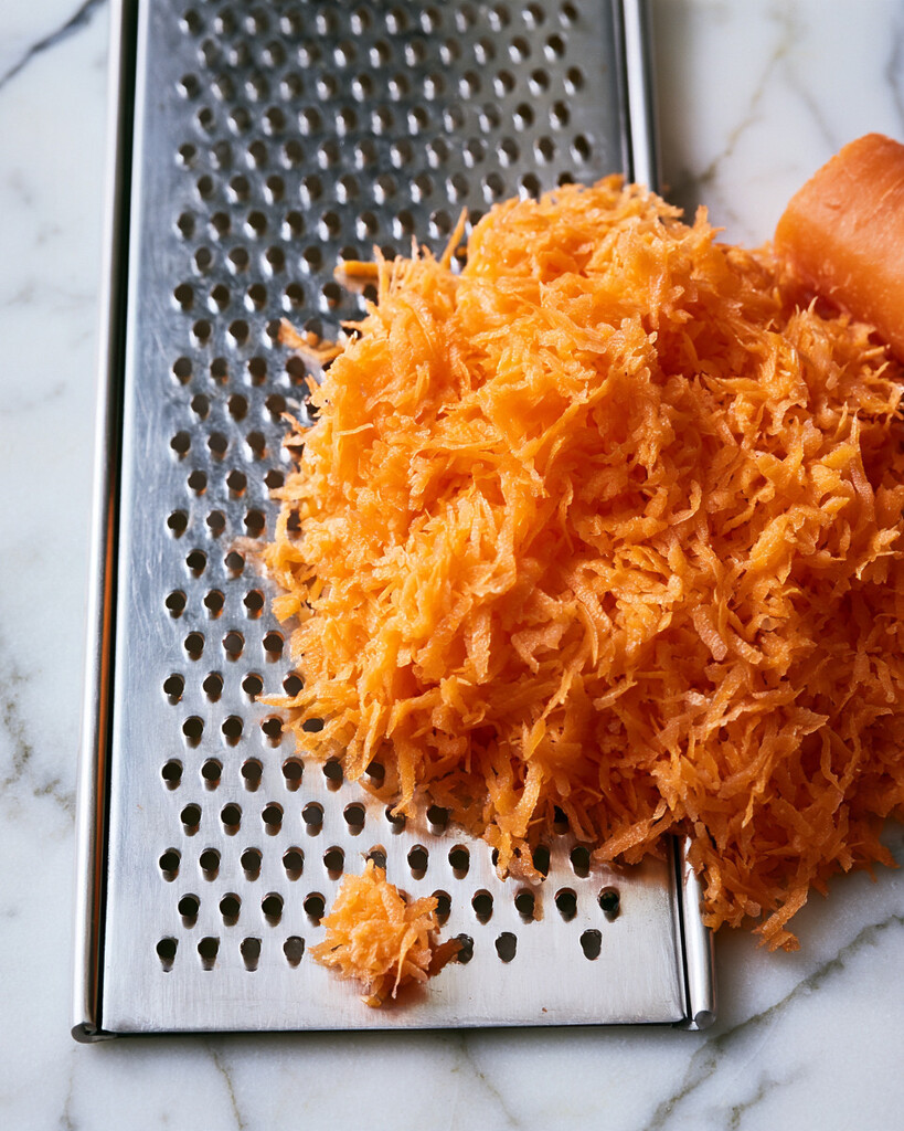 Freshly grated orange carrots piled on a flat metal grater for carrot banana muffin batter